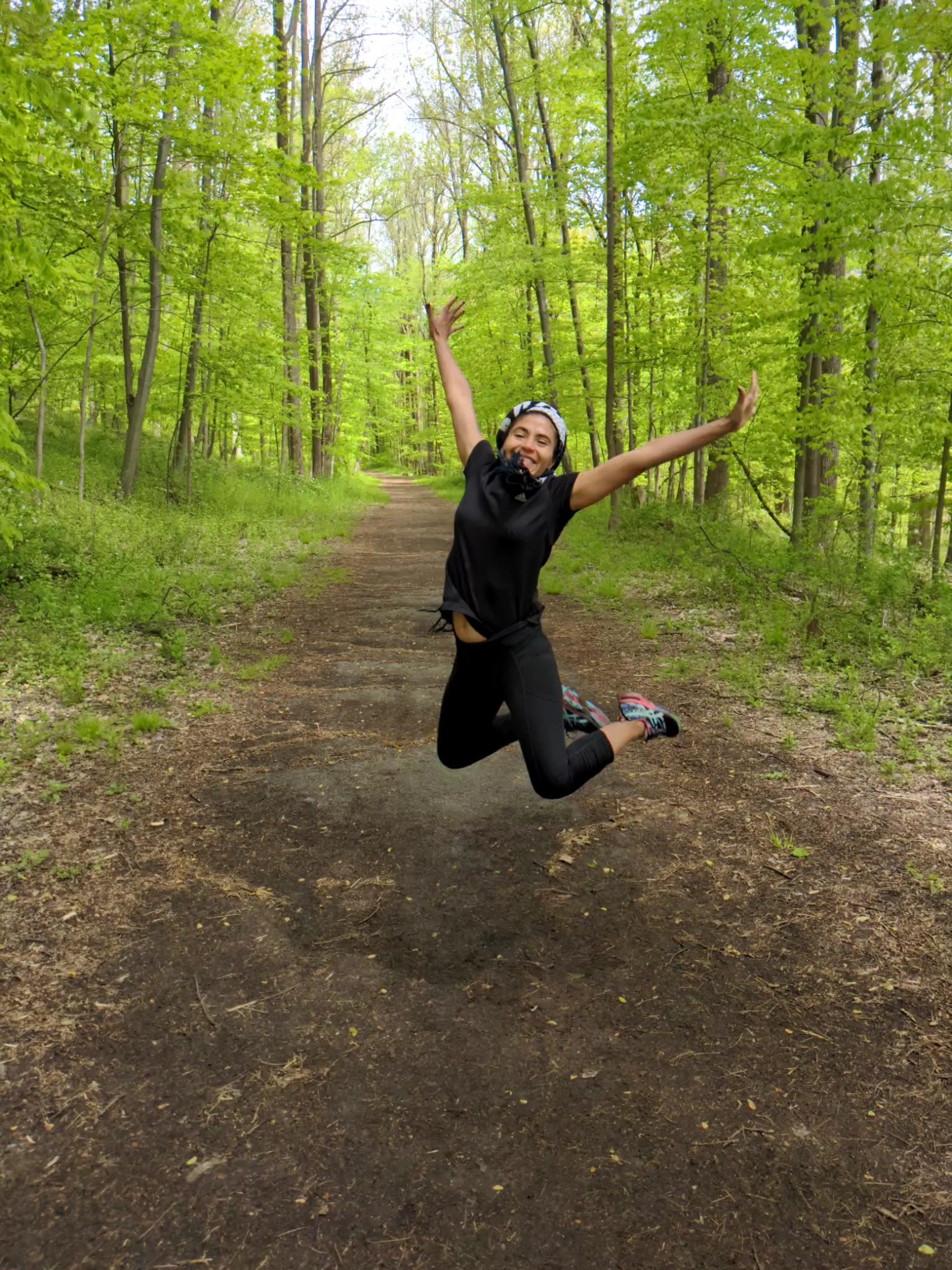 Woman double jumps with arms in the air on a forest trail. Exercise motivation. Holistic fitness. Online personal trainer.